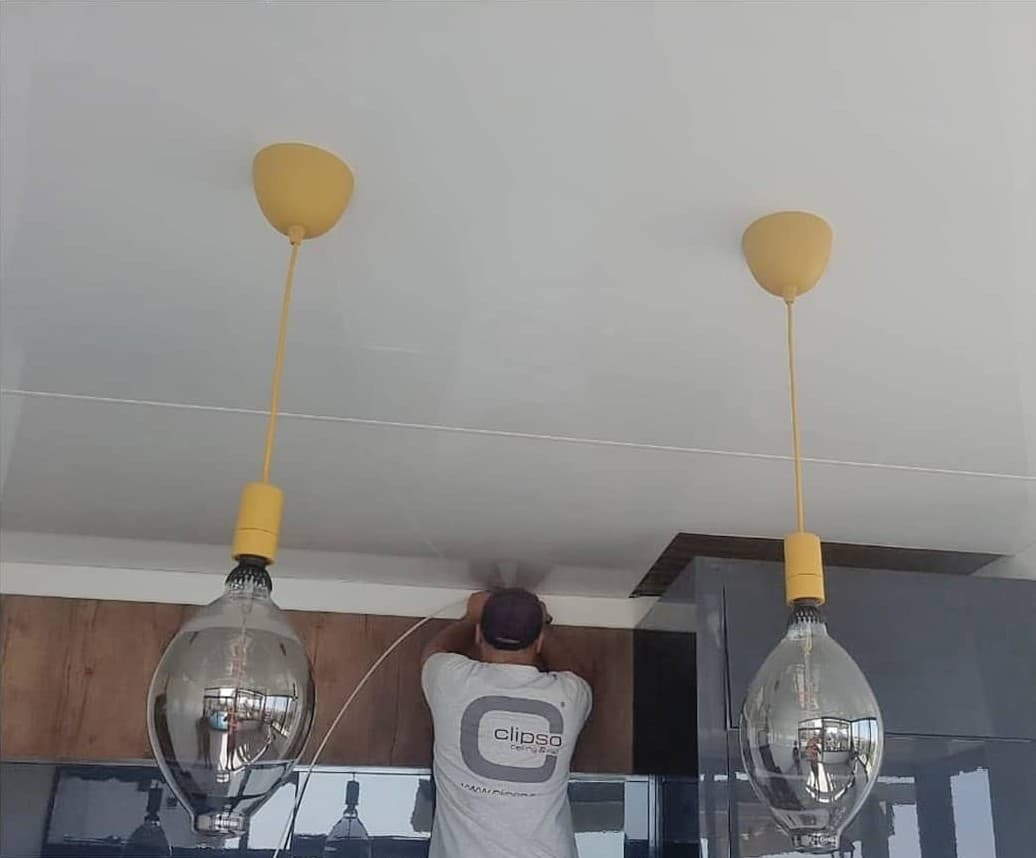 Glossy stretch ceiling installation in progress above pendant lights