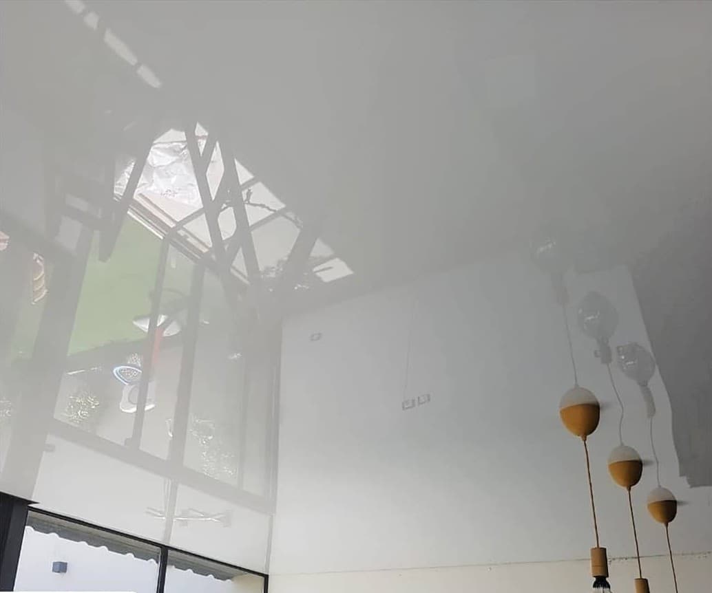 White high-gloss stretch ceiling reflecting the window and room