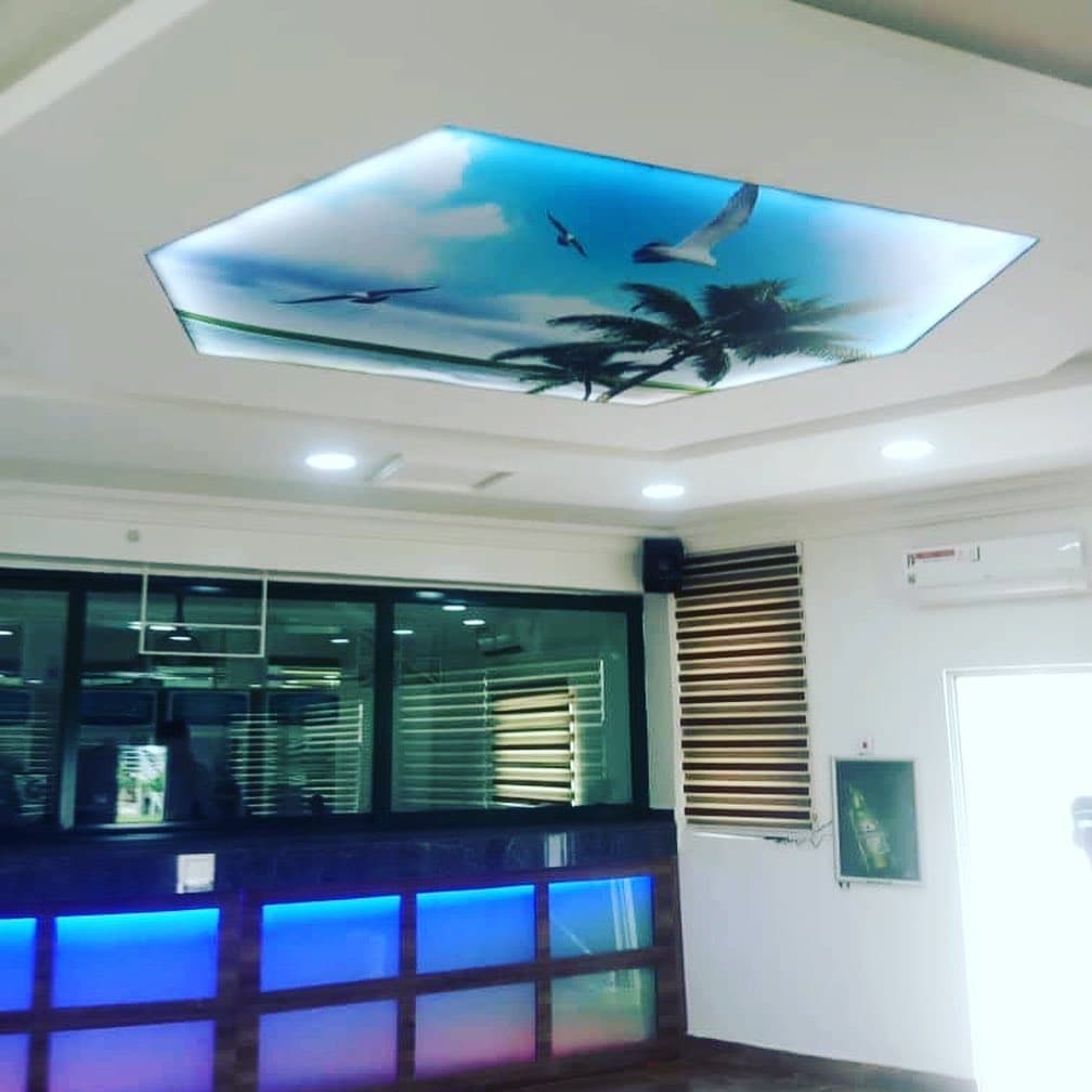 Reception counter with blue accent lighting under a palm-and-sky printed ceiling