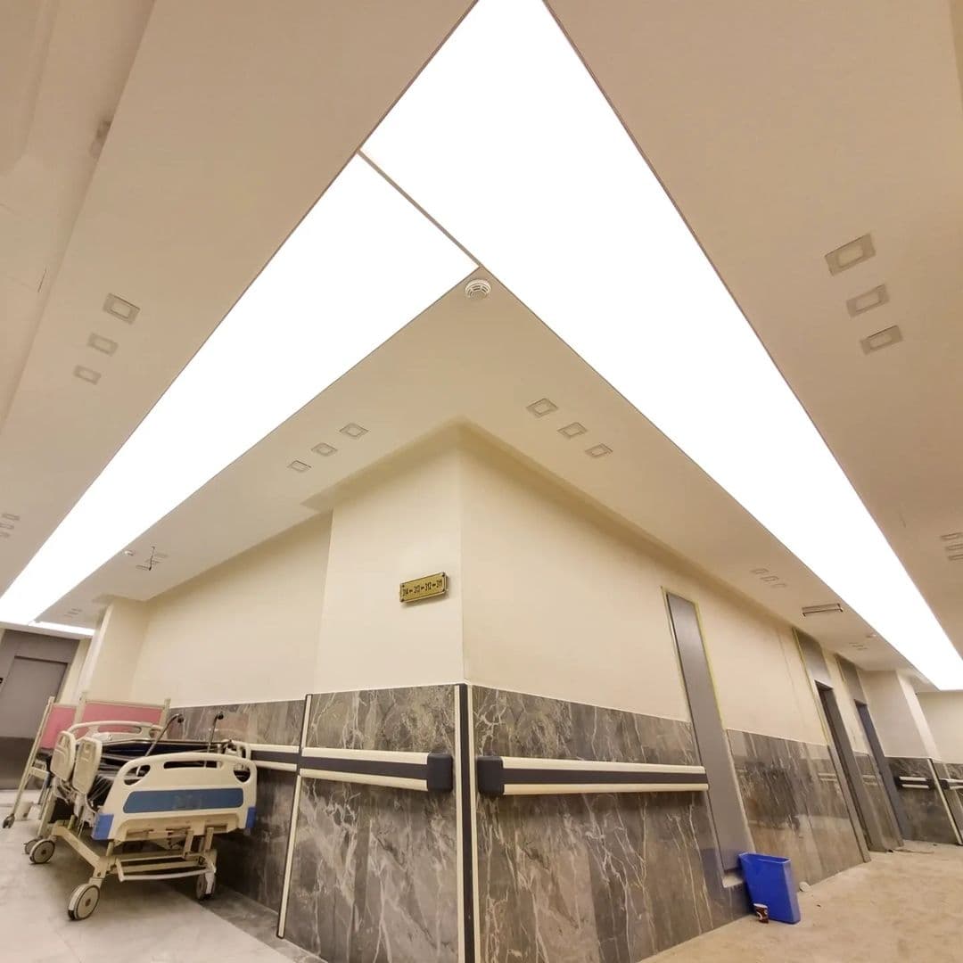 Hospital corridor with a long backlit ceiling line above a patient bed