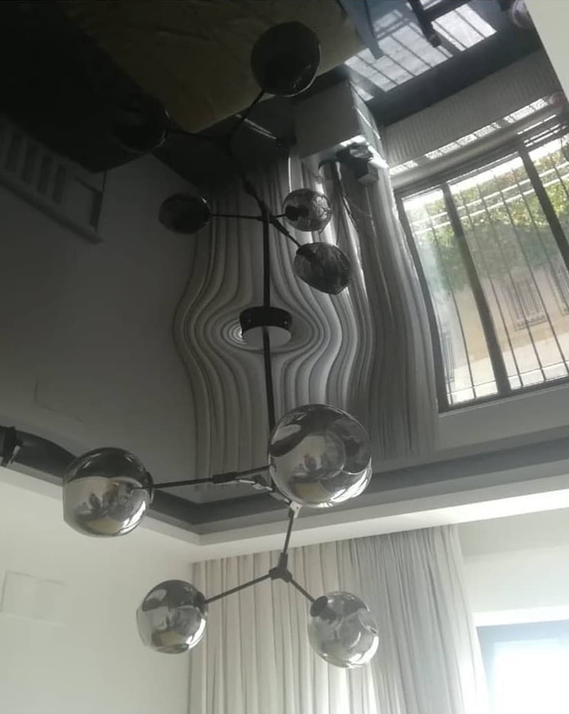 Black high-gloss stretch ceiling reflecting a chandelier